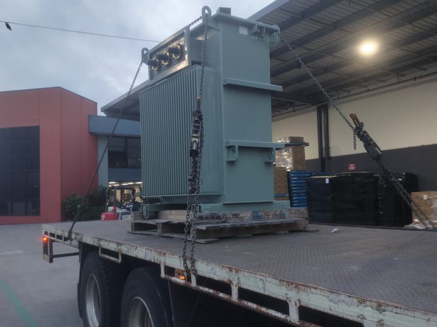 Heavy plant unit loaded by crane onto a TLH flat top at dusk.